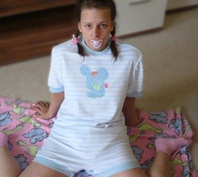 Adult Teen Girl Sitting Down On the Bedsheet while sucking the pacifier