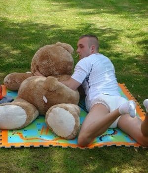 Young man lying asleep in Grass with a teddy bear
